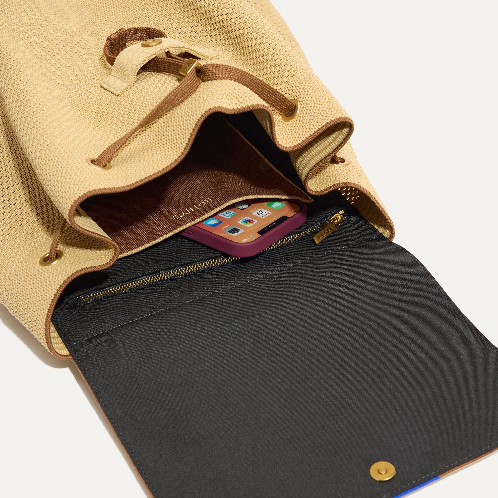 A close up of The Cinch Backpack in Brown Butter showing the interior pockets with a phone inside.