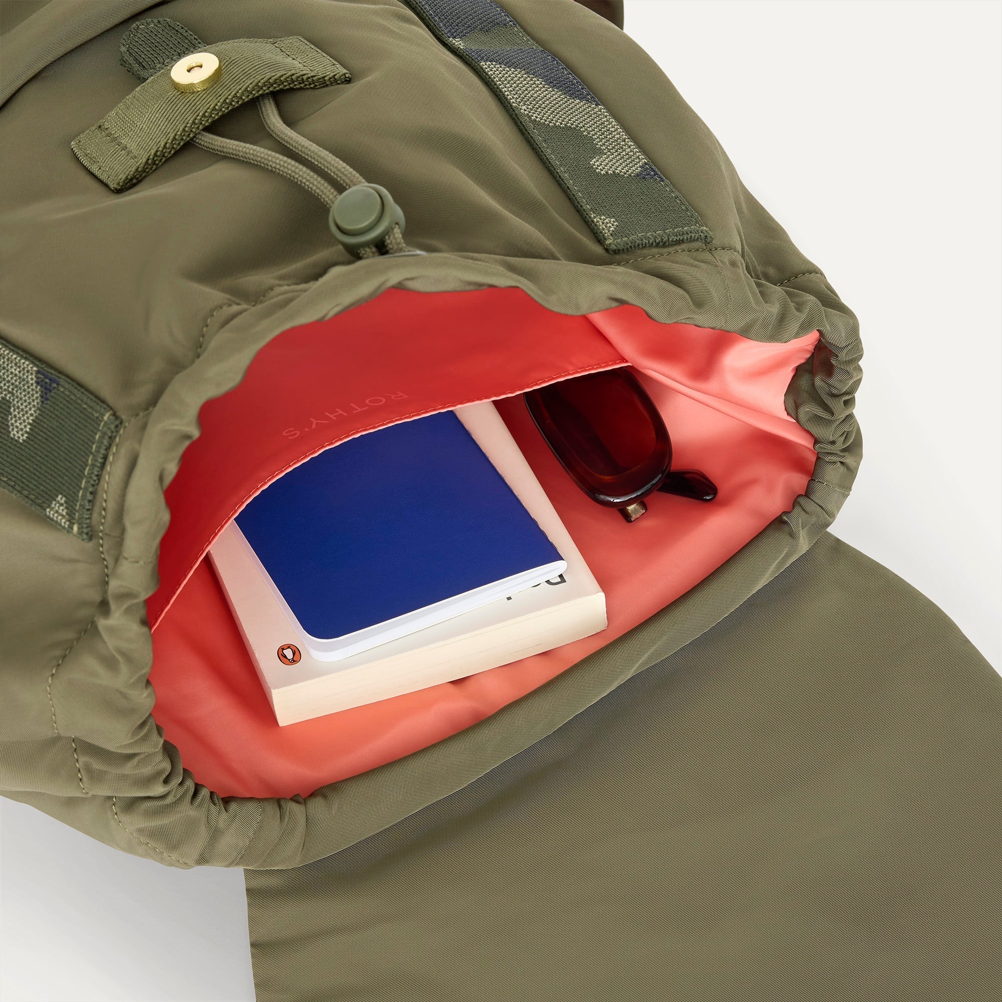 A close up of The Travel Cinch Backpack in Forest showing the interior pockets with a book inside.