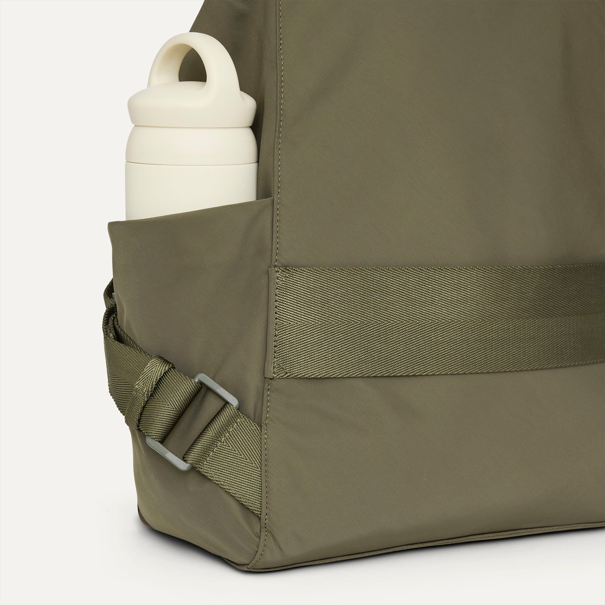 A close up of the The Travel Cinch Backpack in Forest focusing on the straps, and the side pocket.
