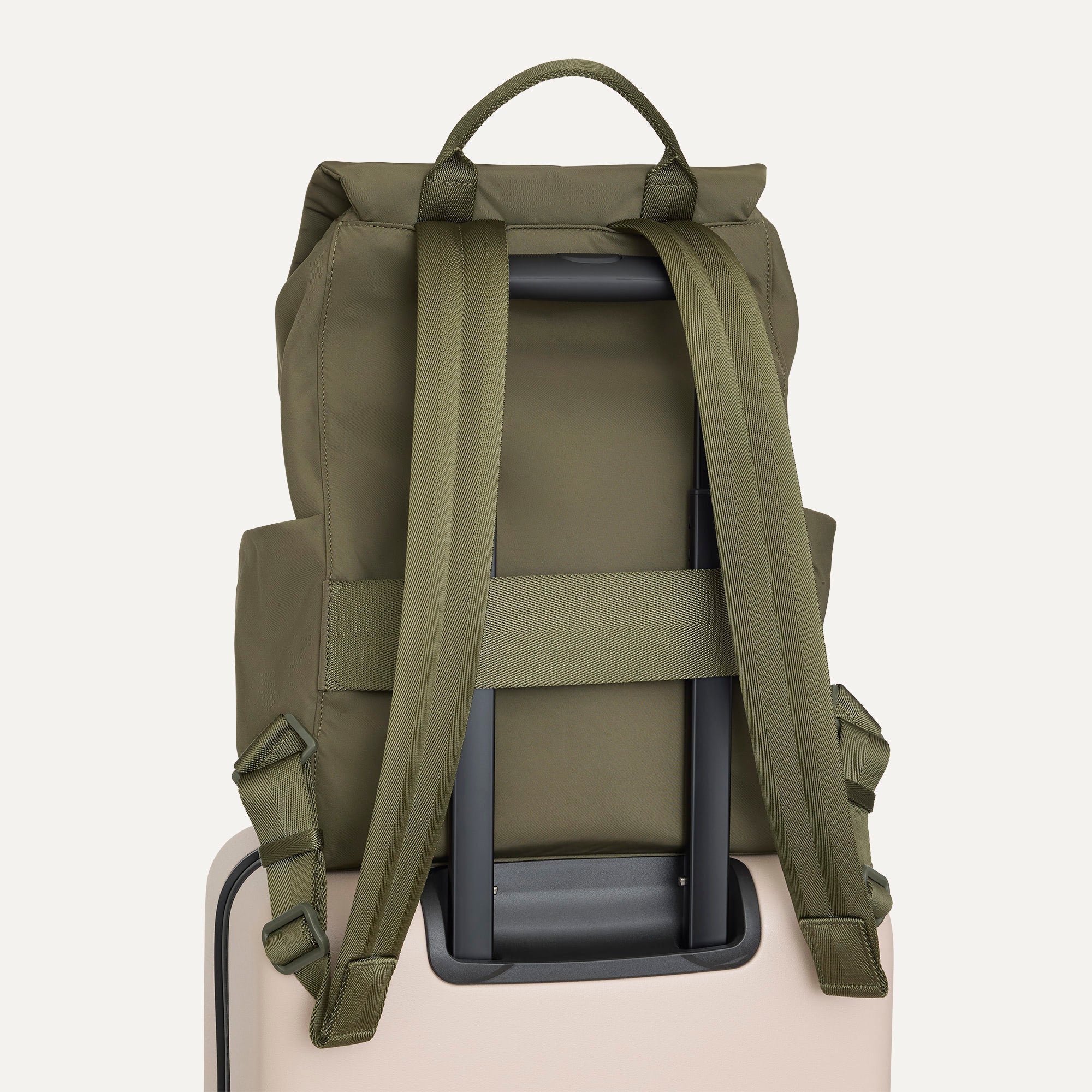 The Travel Cinch Backpack in Forest shown from the back, shown attached to a rolling suitcase using the wrap-around band.