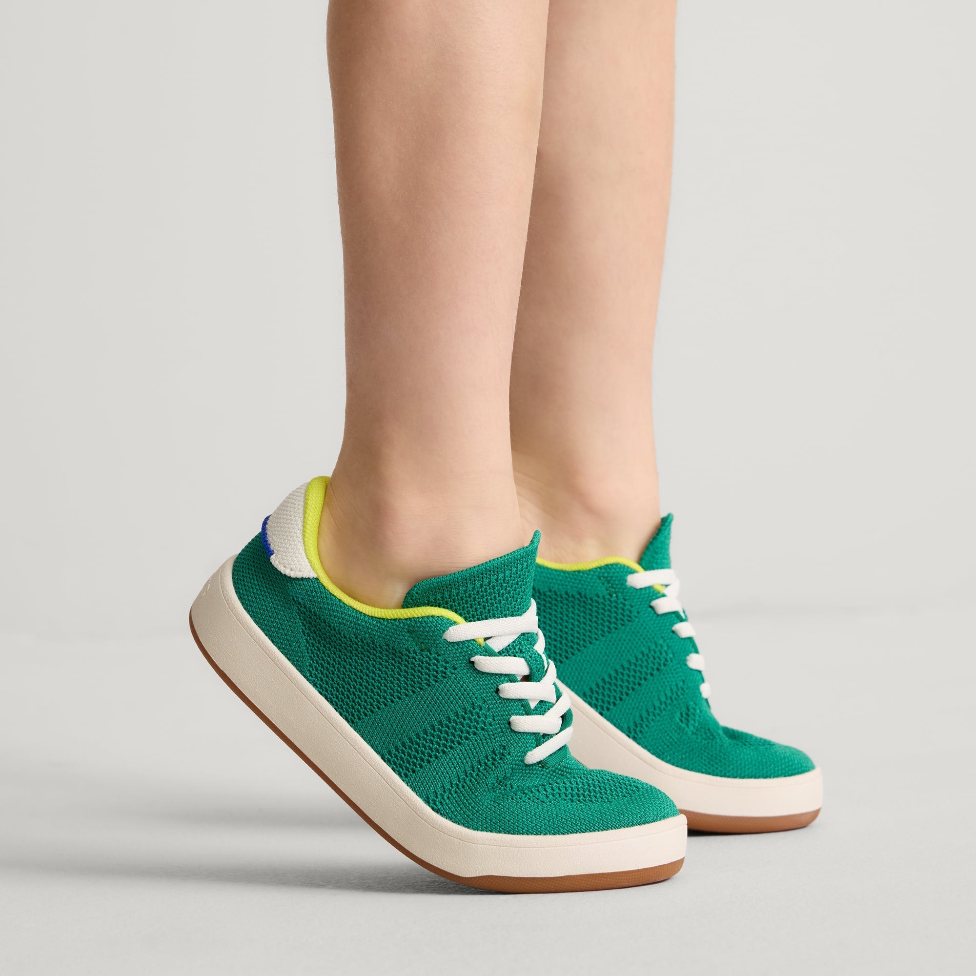 hover | A child modeling The Kids Stretch Sneaker in Emerald Pop.