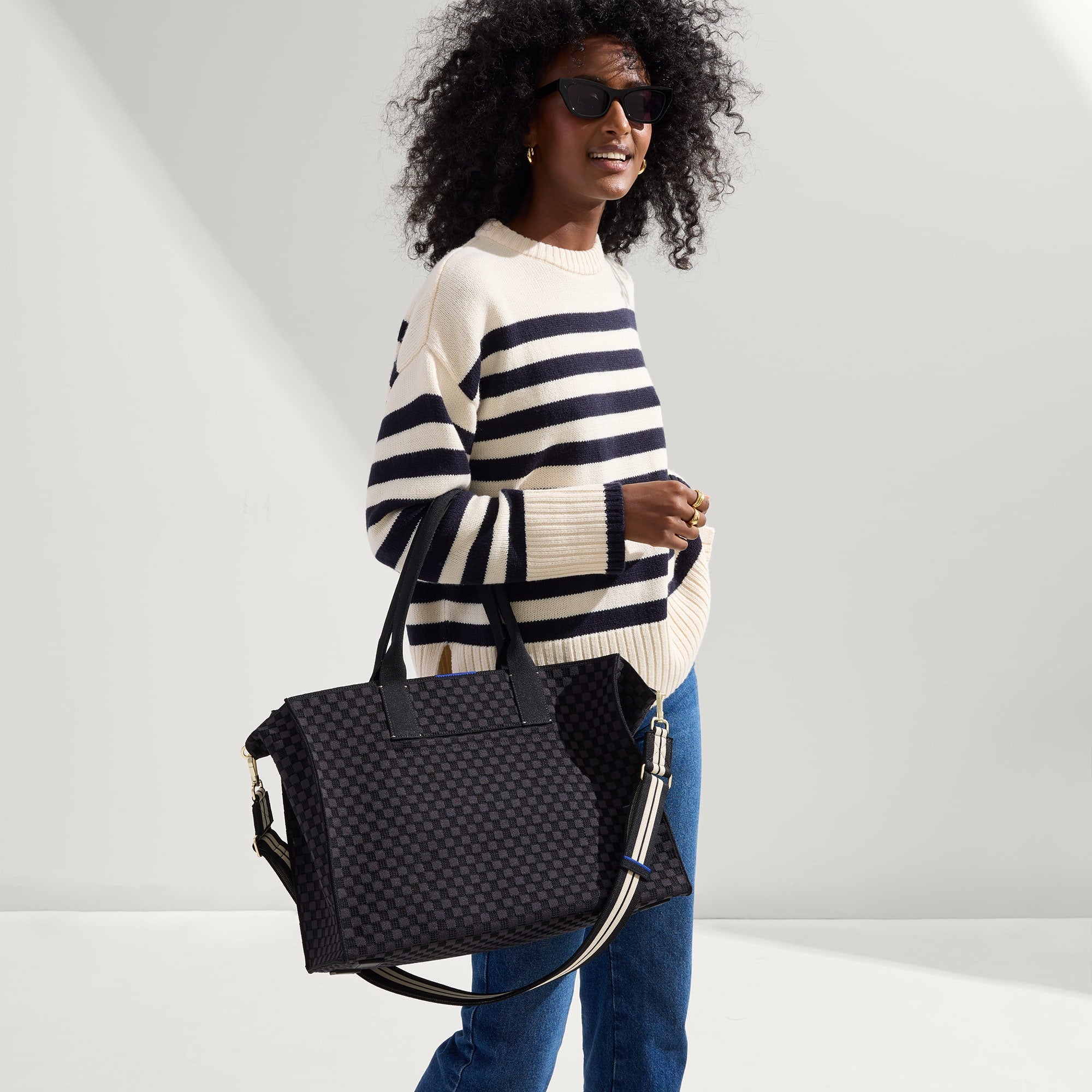 hover | Overlay:: Shown with The Crossbody Strap (sold separately.) | Alt:: The Classic Tote in Black Sand, carried by its top handles by a model, shown from side.